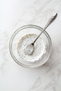 This image shows a creamy dressing being prepared, likely with ingredients like mayonnaise or sour cream, to complement the fresh cucumbers and onions in the salad.