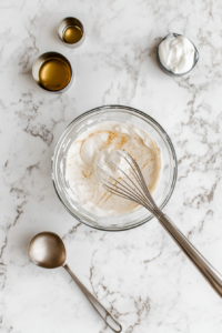 This image shows a creamy dressing being prepared in a mixing bowl with a whisk, combining ingredients for a flavorful base to coat the pea salad.