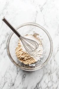 This image shows the dry and wet ingredient mixtures being poured and combined in a bowl to form the cookie dough for low-calorie chocolate chip cookies.