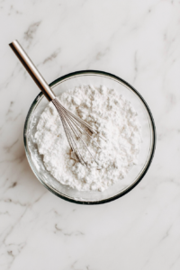 This image shows flour, baking powder, salt, and sugar being combined in a large mixing bowl, forming the dry base for no yeast bread.