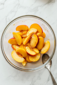 This image shows sliced peaches being gently mixed in a large bowl with cinnamon and a splash of lemon juice to enhance their flavor for the cream pie.