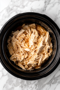 Shredded chicken is added back to the Crockpot and mixed thoroughly with the creamy sauce for even flavor distribution.