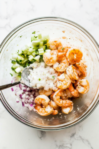 This image shows shrimp pieces being mixed with seasoning and other ingredients in a bowl to create the flavorful shrimp salad topping for cucumber bites.