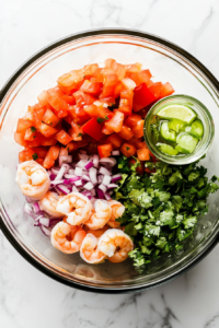 this image shows A bowl with chopped shrimp, tomatoes, onions, and cilantro being combined with lime juice.