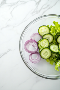 This image shows the freshly sliced cucumbers and onions being combined in a bowl, creating the base for the cucumber salad.