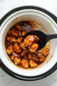 This image shows the cooked orange chicken being carefully transferred from the slow cooker to a serving plate, ready for garnishing.