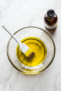 This image shows a mixing bowl being brushed with oil to prevent the dough from sticking during the rising process.