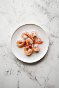 This image depicts thawed shrimp being carefully patted dry with a paper towel to remove excess moisture before further preparation.