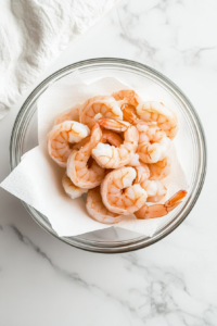 This image shows shrimp being gently dried with paper towels to remove excess moisture, allowing for better seasoning and even cooking.