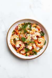 This image shows pickled shrimp served on a white round plate, beautifully garnished with fresh herbs, ready to enjoy as a flavorful appetizer or side dish.