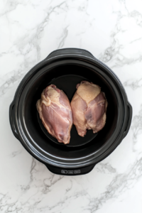 This image shows raw chicken breasts being placed in a slow cooker, forming the base of the Crockpot White Chicken Chili recipe.