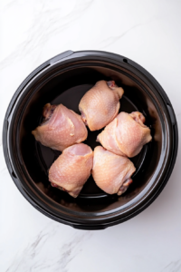 This image shows raw chicken thighs being carefully placed into a slow cooker, ready to be cooked for the honey garlic chicken recipe.