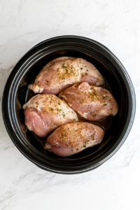 Seasoned chicken breasts being carefully layered into the crockpot, forming the first step in cooking the Tuscan Chicken recipe.