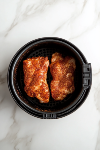 This image shows seasoned chicken breasts being carefully placed into the air fryer basket, ready to cook to golden perfection.