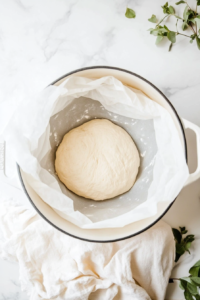 This image shows the shaped dough being carefully lowered into the preheated Dutch oven, ready to bake into a crusty artisan loaf.