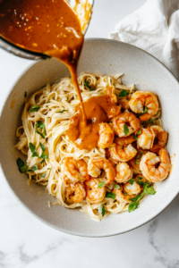 This image shows the creamy Bang Bang sauce being poured generously over a skillet of cooked shrimp and pasta, adding rich flavor to the dish.