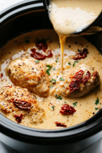 Rich and creamy Tuscan sauce being poured over the layered chicken breasts in the crockpot, ensuring even coverage for the slow-cooking process.