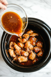 This image shows the prepared honey garlic sauce being poured over chicken thighs in a slow cooker, ensuring the chicken is fully coated for flavorful cooking.