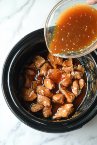 This image shows the prepared orange sauce being poured over the chicken pieces in the slow cooker, covering them evenly.