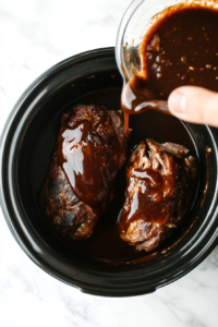 this image shows A close-up of the rich, savory sauce being poured over a pork tenderloin sitting in a slow cooker, evenly coating the meat for maximum flavor.