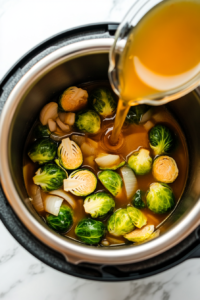 This image shows vegetable broth being poured into the Instant Pot, creating a flavorful base for the Brussels sprouts to cook in.