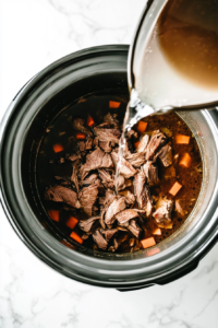 This image shows water being carefully poured into the slow cooker, blending with the onion soup mix and roast to create a flavorful cooking liquid.