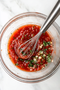 This image shows a glass bowl containing honey, garlic, soy sauce, and other seasonings being whisked together to create a flavorful sauce for the chicken.