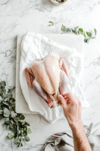 This image shows a raw turkey breast being rinsed under water and then patted dry with a paper towel in preparation for cooking.