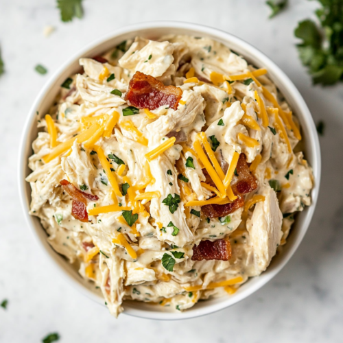 This image shows a hearty bowl of protein-packed carnivore chicken salad, featuring shredded chicken mixed with seasoned mayo, crispy bacon, and shredded cheese, served in a white bowl as a satisfying dish.