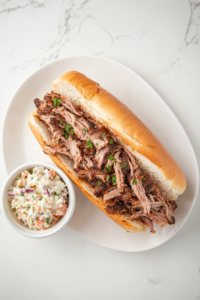 This image shows a completed pulled pork sandwich served on a plate with a side of creamy coleslaw, ready to be enjoyed as a hearty and flavorful meal.