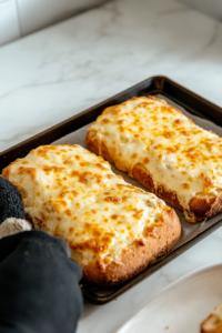 baking sheet being carefully removed from the broiler, showing the cheese bread with a golden, bubbly topping.