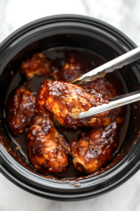 Tender and juicy BBQ chicken being carefully lifted out of the slow cooker, ready for shredding and mixing with sauce.