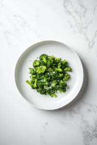 This image shows a pair of tongs lifting freshly sautéed broccoli from the skillet, placing it aside on a plate to make room for the shrimp.