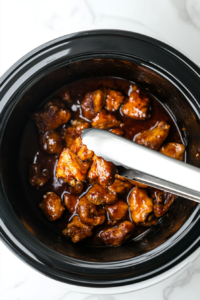 This image shows cooked chicken thighs being carefully removed from the slow cooker, tender and infused with the flavors of the honey garlic sauce.