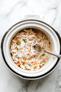 This image shows the shredded chicken being added back to the crockpot, combining with the creamy vegetable gravy to complete the filling for the chicken pot pie.