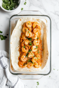 This image shows a tortilla being tightly rolled with its shrimp filling, forming perfect enchiladas ready to be placed in a baking dish.