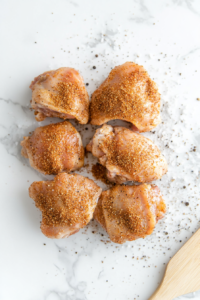 A pair of hands rubbing a flavorful seasoning mixture onto raw chicken breasts, ensuring even coating for a rich and spiced flavor in the keto chicken dish.