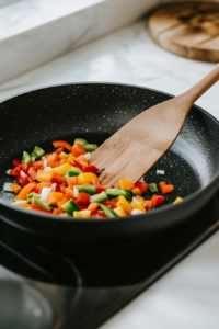 This image shows bell peppers and onions sizzling in a skillet with olive oil, releasing their natural flavors for the creamy curry dish.