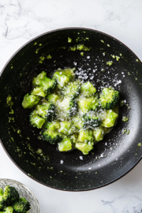 This image shows vibrant green broccoli florets being sautéed in a hot skillet with a light coating of butter and oil, creating a flavorful foundation for the dish.