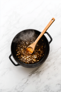 This image shows diced onion and minced garlic being sautéed in a skillet, releasing their aromatic flavors as the base for vegan broccoli cheese soup.