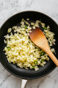 This image shows onions and jalapeños being sautéed in a pan, creating a fragrant and spicy base for the creamy queso dip.