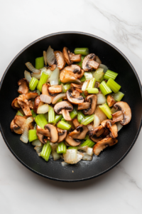 This image shows a mixture of vegetables being sautéed in the skillet, developing savory flavors for the casserole filling.