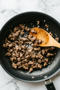 This image shows the cooked sausage in a skillet being seasoned with a mix of spices and herbs to enhance the flavor for the lasagna filling.