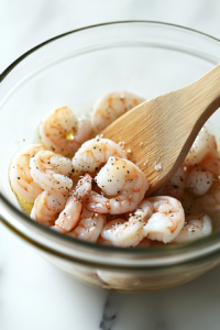 This image shows large shrimp being tossed with olive oil, salt, and pepper, ready to be cooked for the salad.