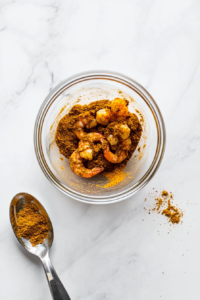 This image shows shrimp being coated with a blend of spices in preparation for making the Jamaican creamy curry, highlighting vibrant and aromatic seasonings.