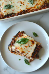 this image shows This image shows a perfectly sliced piece of Keto Eggplant Lasagna being served, with the cheesy, creamy layers visible and garnished with fresh basil.