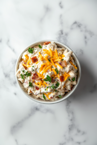 This image shows the finished carnivore chicken salad served in a white bowl, topped with visible bacon pieces and shredded cheese for a visually appealing and protein-rich dish.