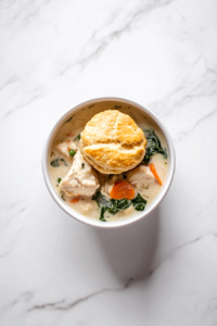 This image shows the creamy chicken pot pie being served warm in a bowl, topped with a freshly baked biscuit for a hearty and satisfying meal.