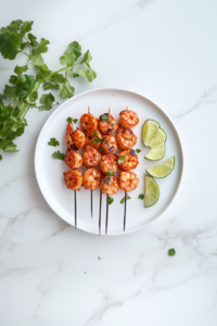 Grilled tandoor shrimp served on a white plate, garnished with chopped cilantro and lime wedges, ready to be enjoyed.