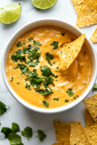 This image shows a rich and creamy queso dip served in a white bowl, garnished with fresh cilantro, perfect for dipping chips or as a flavorful addition to any meal.